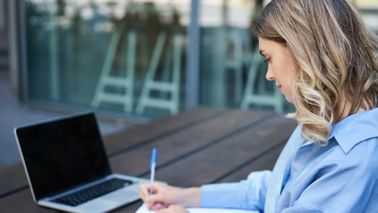 Mujer estudiante tomando apuntes frente a un ordenador portatil